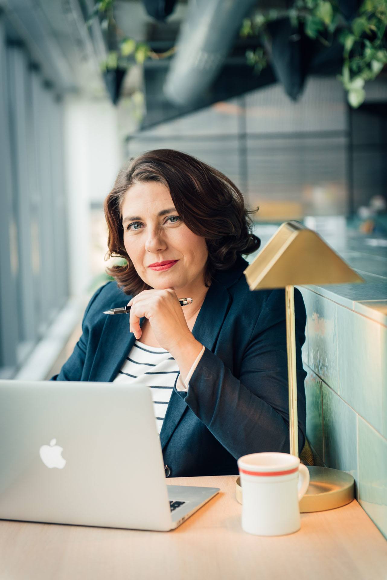 eine weibliche Coachin und Trainerin sitzt mit Laptop und Stift in einem Coworking Space